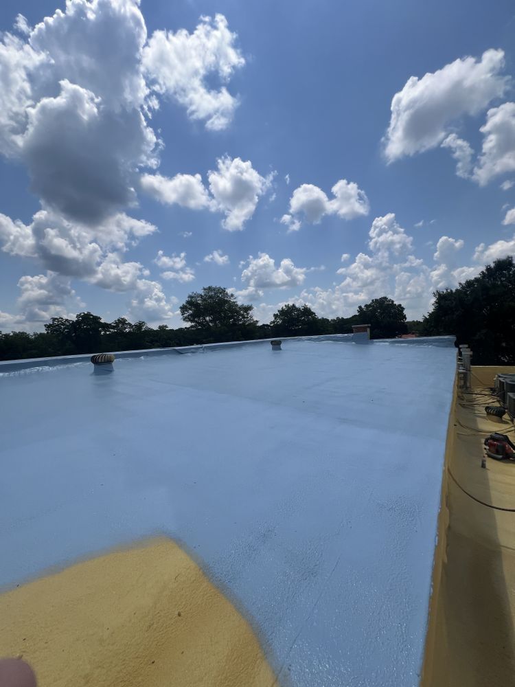 A light blue coated flat roof under a blue sky with fluffy clouds. Trees are in the background.