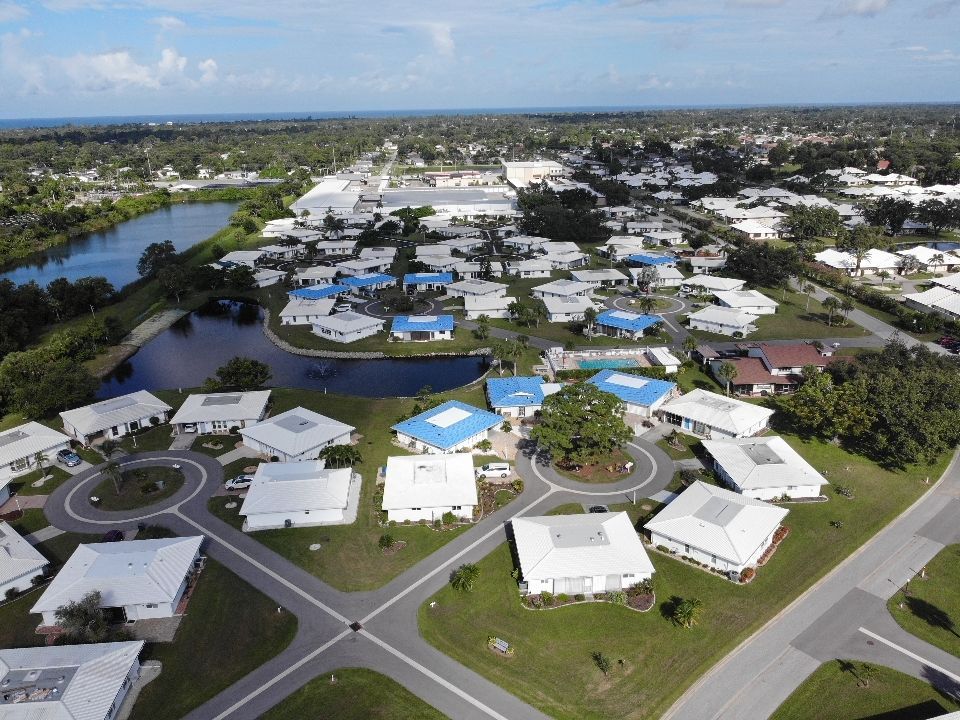 Aerial view of a suburban neighborhood with white houses, blue roofs, and a pond.