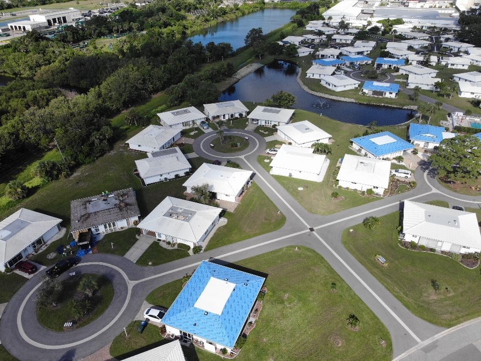 Aerial view of a suburban neighborhood with white houses, blue roofs, and a central pond.