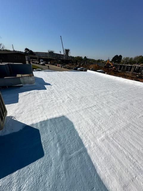 White coated roof, possibly recently applied. Construction site in the background under blue sky.