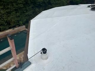 White rooftop with a vent and a black cable, overlooking water and trees.