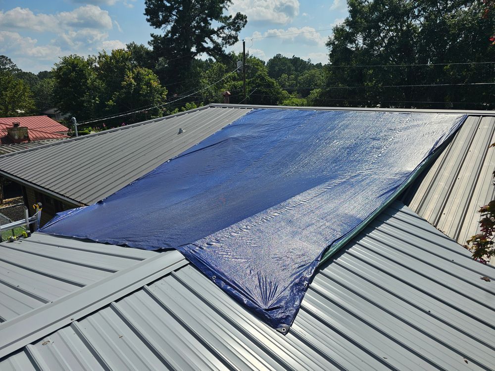 Blue tarp covering a section of a metal roof on a sunny day.