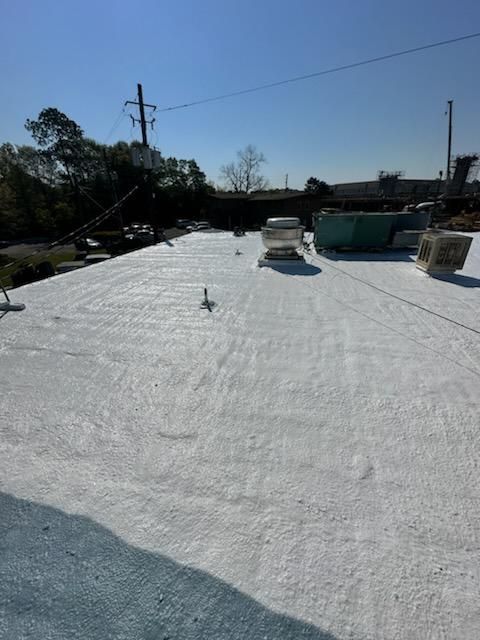 White roof surface with vents, trees, and power lines under a clear blue sky.
