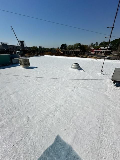 White-coated rooftop on a sunny day with a clear blue sky, a vent, and surrounding buildings visible.