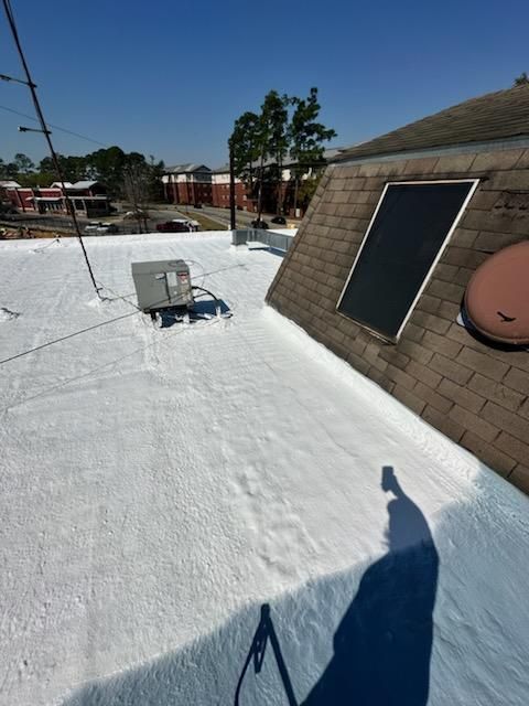 White-coated flat roof with HVAC unit and dormer with solar panel. Clear blue sky overhead.