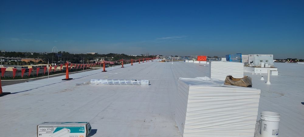 View of a white roof with safety cones, a clear blue sky, and a distant cityscape on a sunny day.