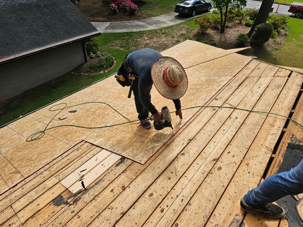 Roofer on a roof, installing wooden panels with a nail gun. Light brown wooden roof, clear blue sky, sunny day.