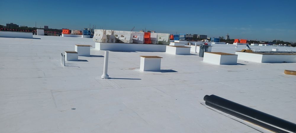 View of a white flat roof with vent pipes and equipment, under a blue sky.