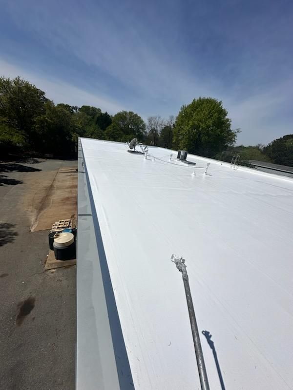 White commercial flat roof on a sunny day. Metal fixtures, blue sky, and trees in background.