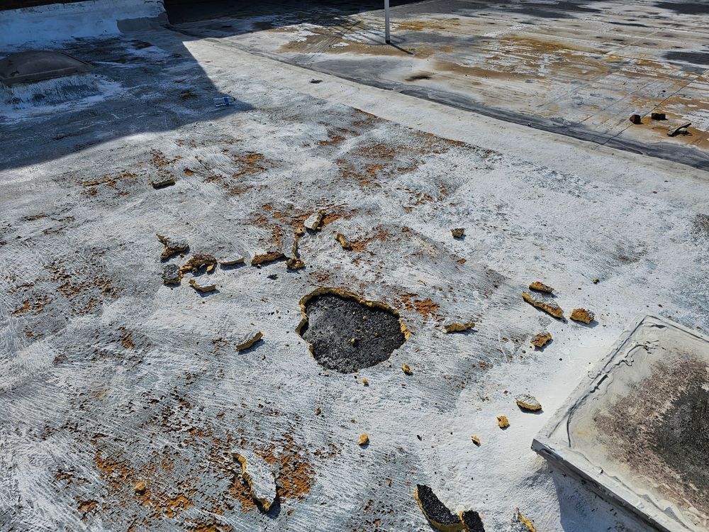 Damaged, white-coated rooftop with a dark hole and scattered debris; setting is outdoors.