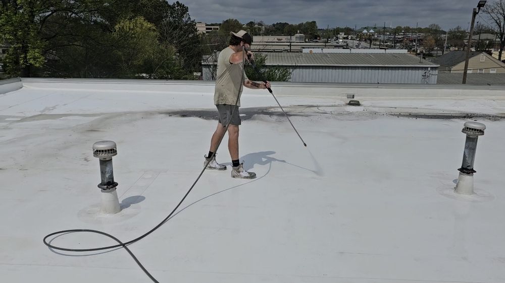 Person spraying white roof with hose on a sunny day.