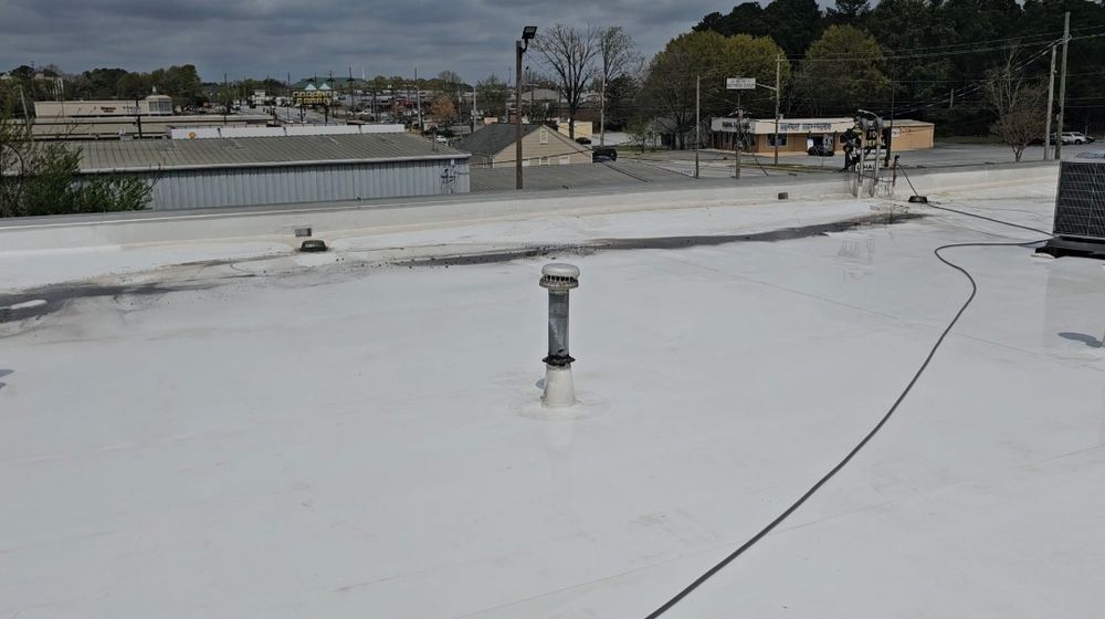 White commercial roof with a vent pipe and buildings in the background under a cloudy sky.