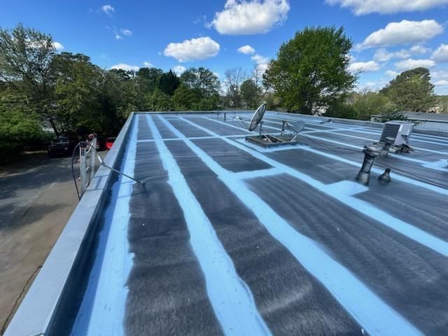 Flat commercial roof with dark, textured surface and blue sealant, under a partly cloudy sky.