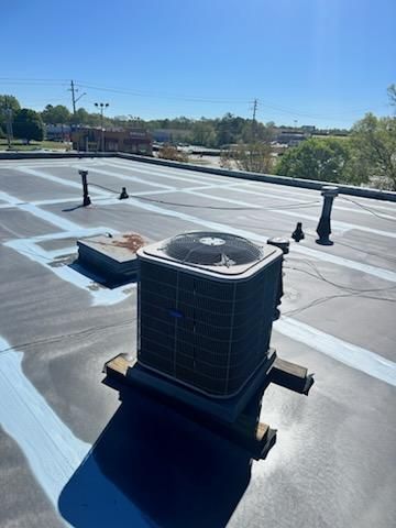 Air conditioning unit on a flat commercial roof with blue stripes, against a bright sky.