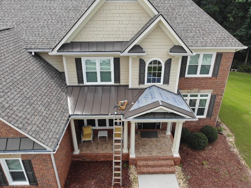 Brick house with brown and beige siding, brown roof, and a ladder leaning against the porch.