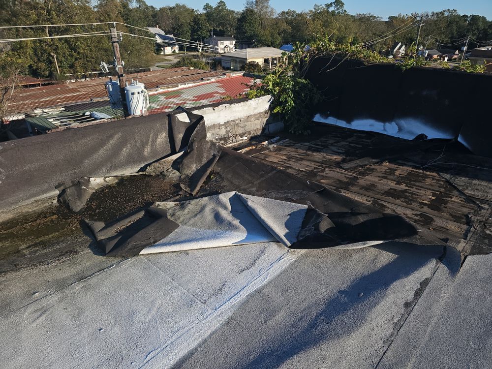 Damaged flat roof with peeling black membrane, revealing white underlayment.