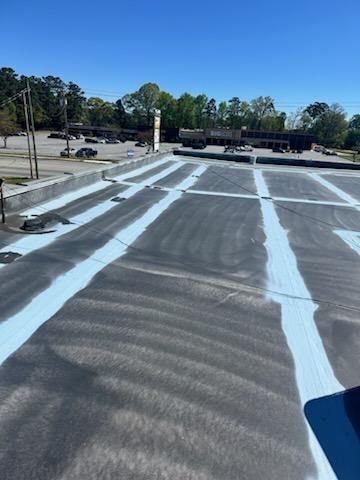 A flat commercial roof with blue stripes, viewed from a high angle. Buildings and trees are in the background.