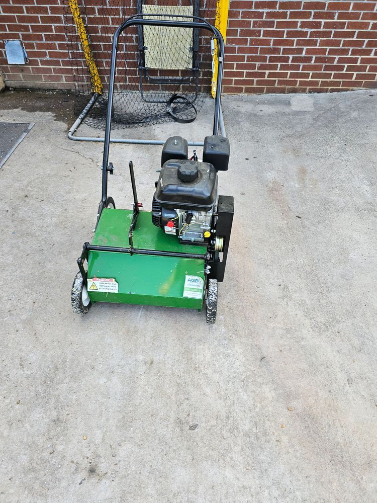 Green and black lawn dethatcher with a brick wall background.