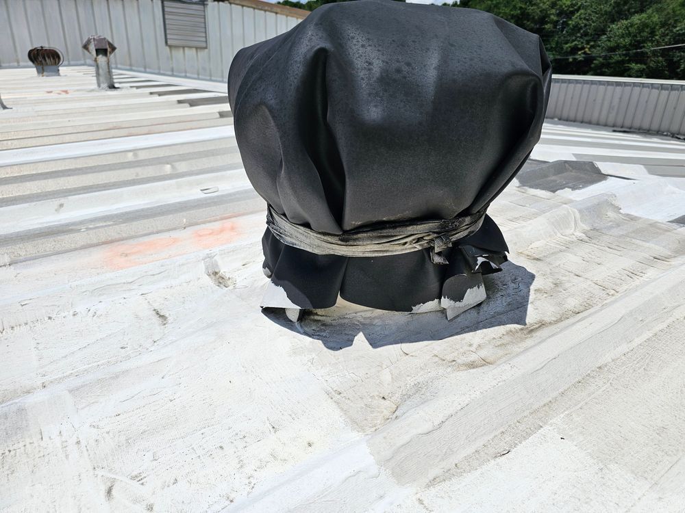 Black covered vent on a white commercial roof. Other vents and building in the background. Sunny day.