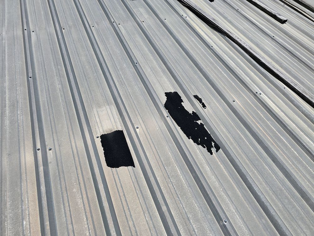Damaged metal roof with large patches of missing coating, revealing the dark underlayer.