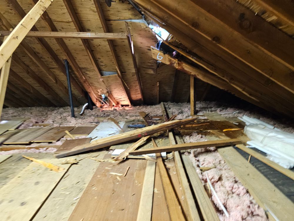 Interior view of an attic with damaged wooden structure and insulation visible.