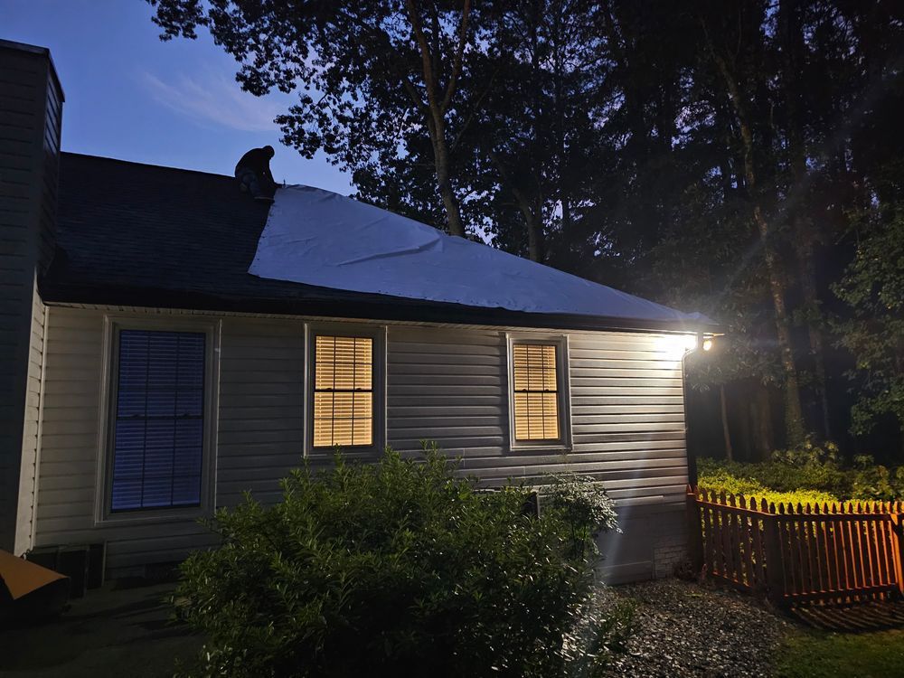 Night view of a house with lit windows and a partial solar panel. A cat sits on the roof.