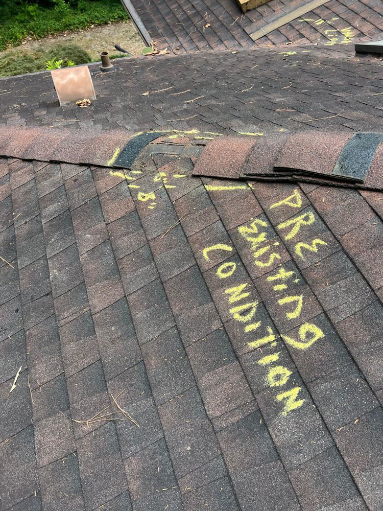 Close-up of a dark brown shingle roof with yellow spray-painted words 