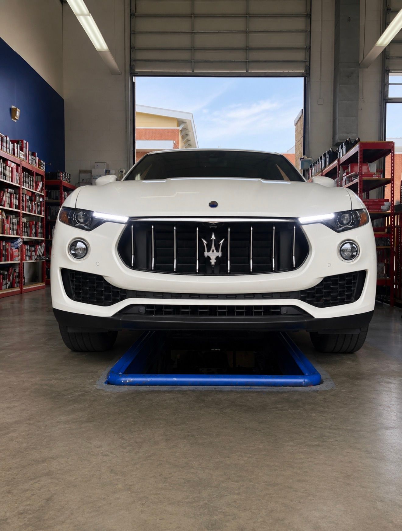 White Maserati SUV parked inside a garage on a blue lift platform, front view