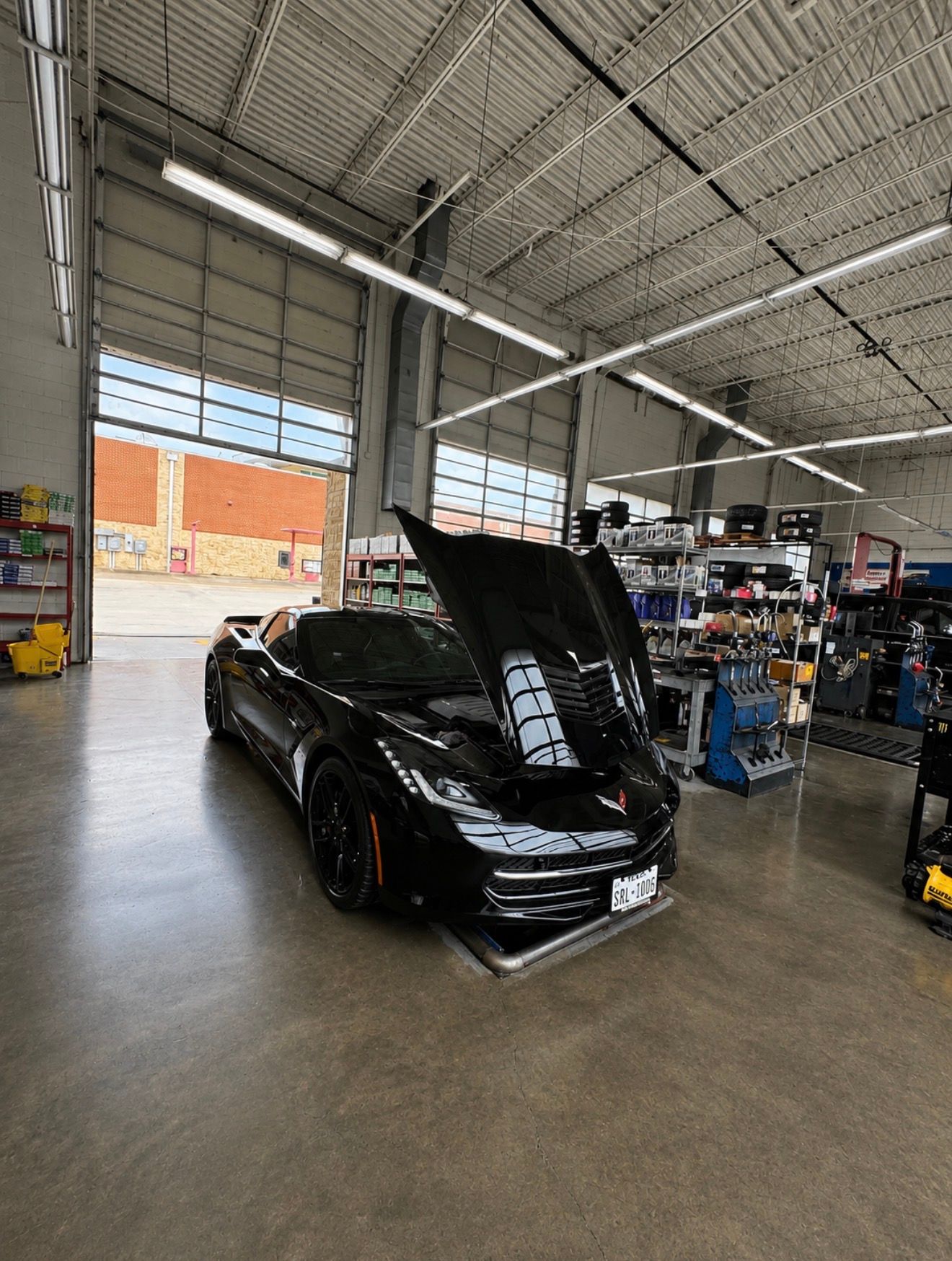 Black sports car with hood open inside an auto shop garage.