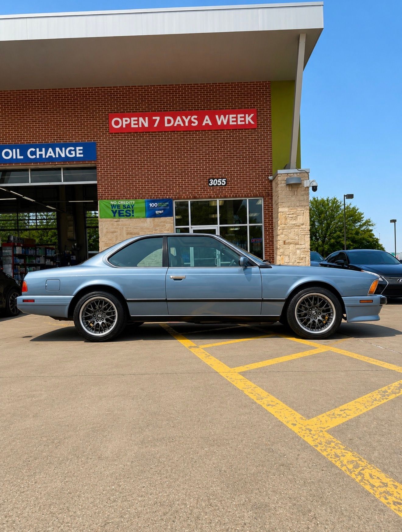 Blue classic car parked outside an oil change shop with an “Open 7 Days a Week” sign