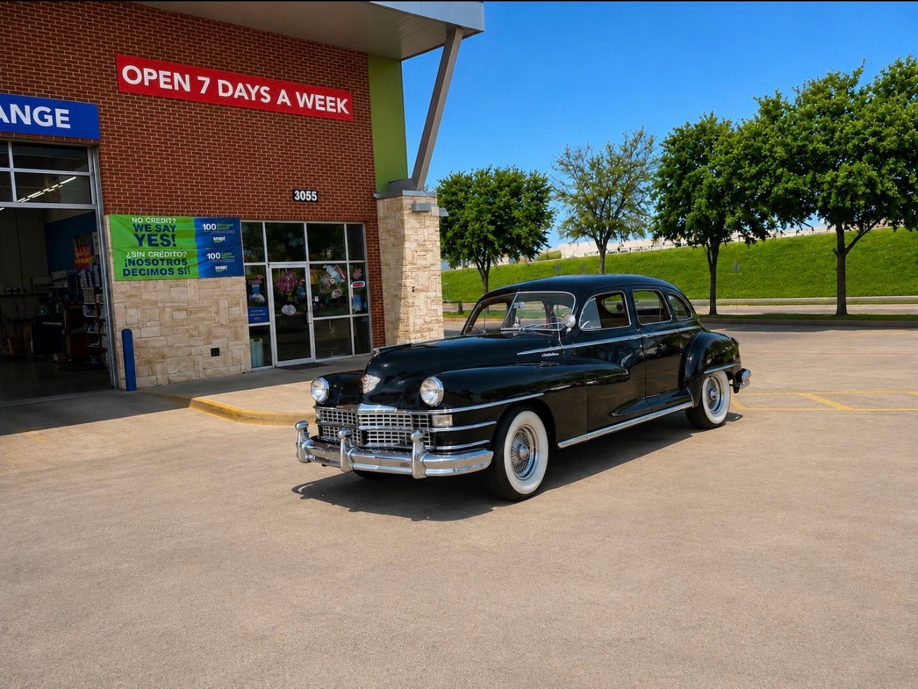 Black vintage car parked outside a store with an “Open 7 days a week” sign