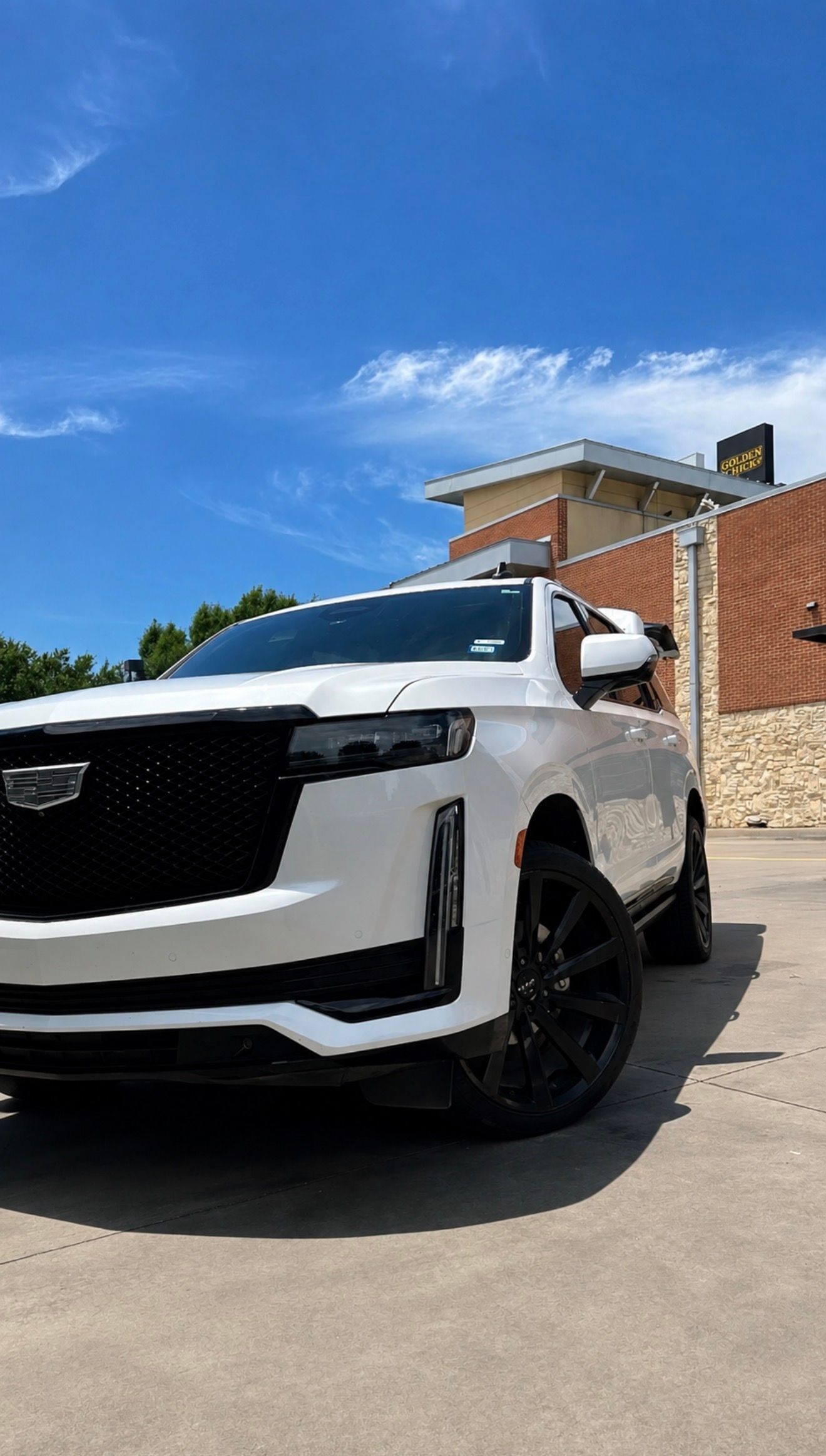 White SUV parked on a sunny lot beside a brick wall and blue sky