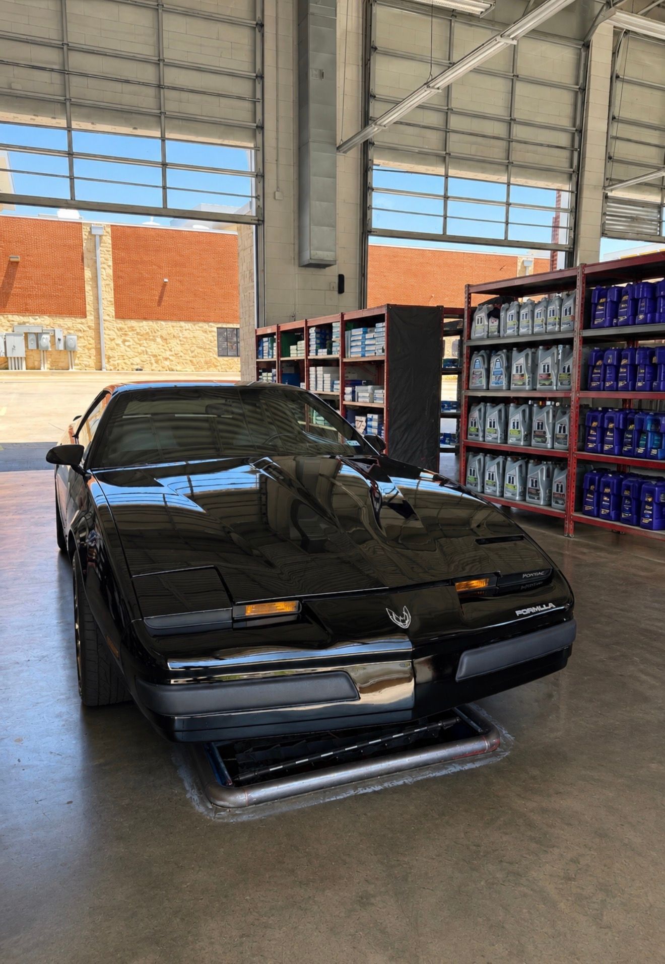 Black sports car parked inside a warehouse-like garage with shelves and windows.