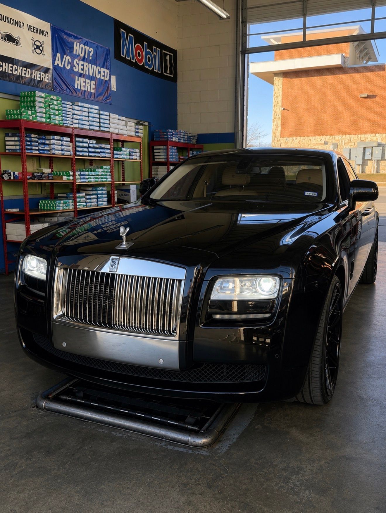 Black Rolls-Royce parked indoors at a car wash or service bay, front view.