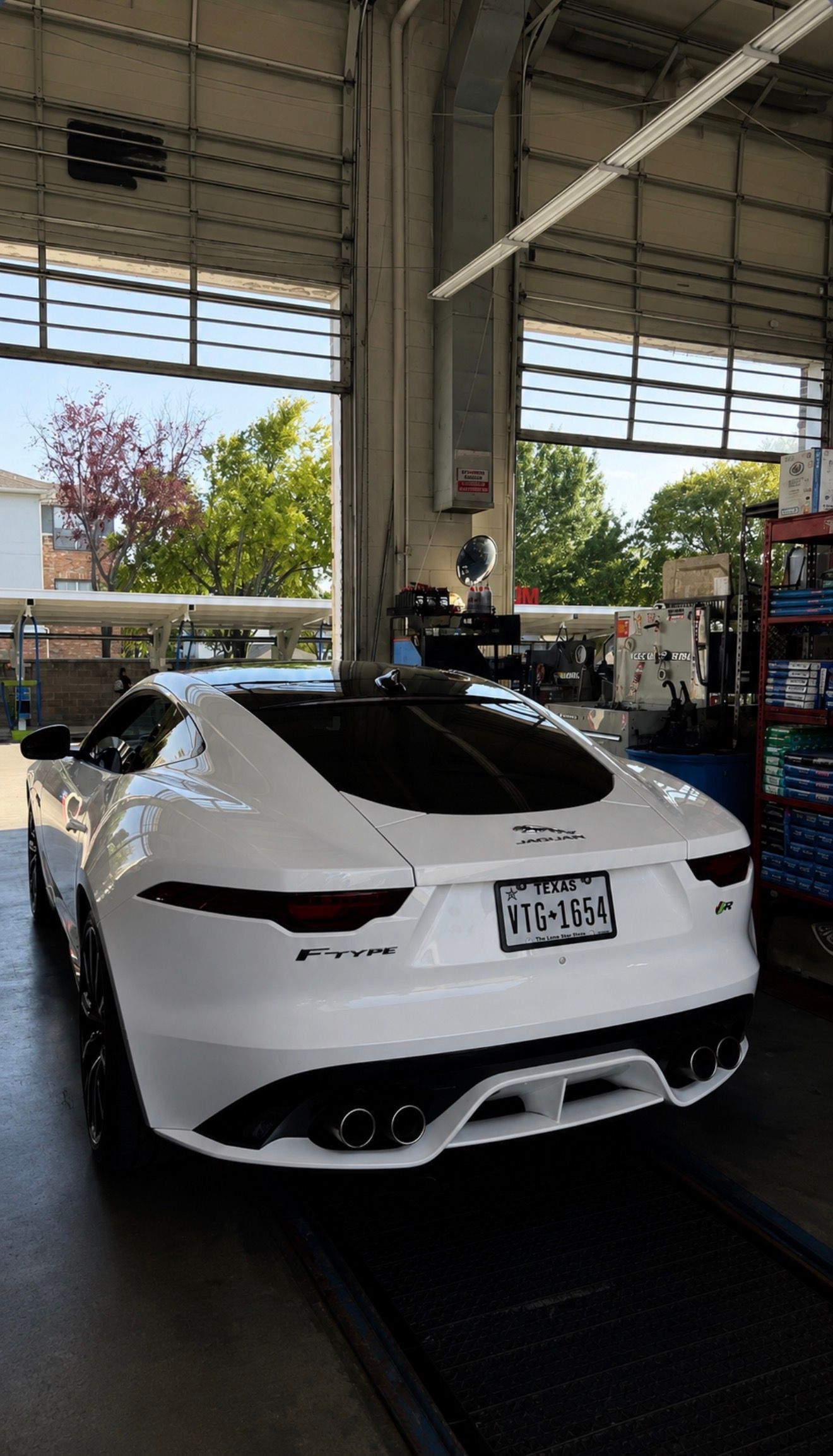 White sports car parked inside an auto service garage with large open bays and daylight outside
