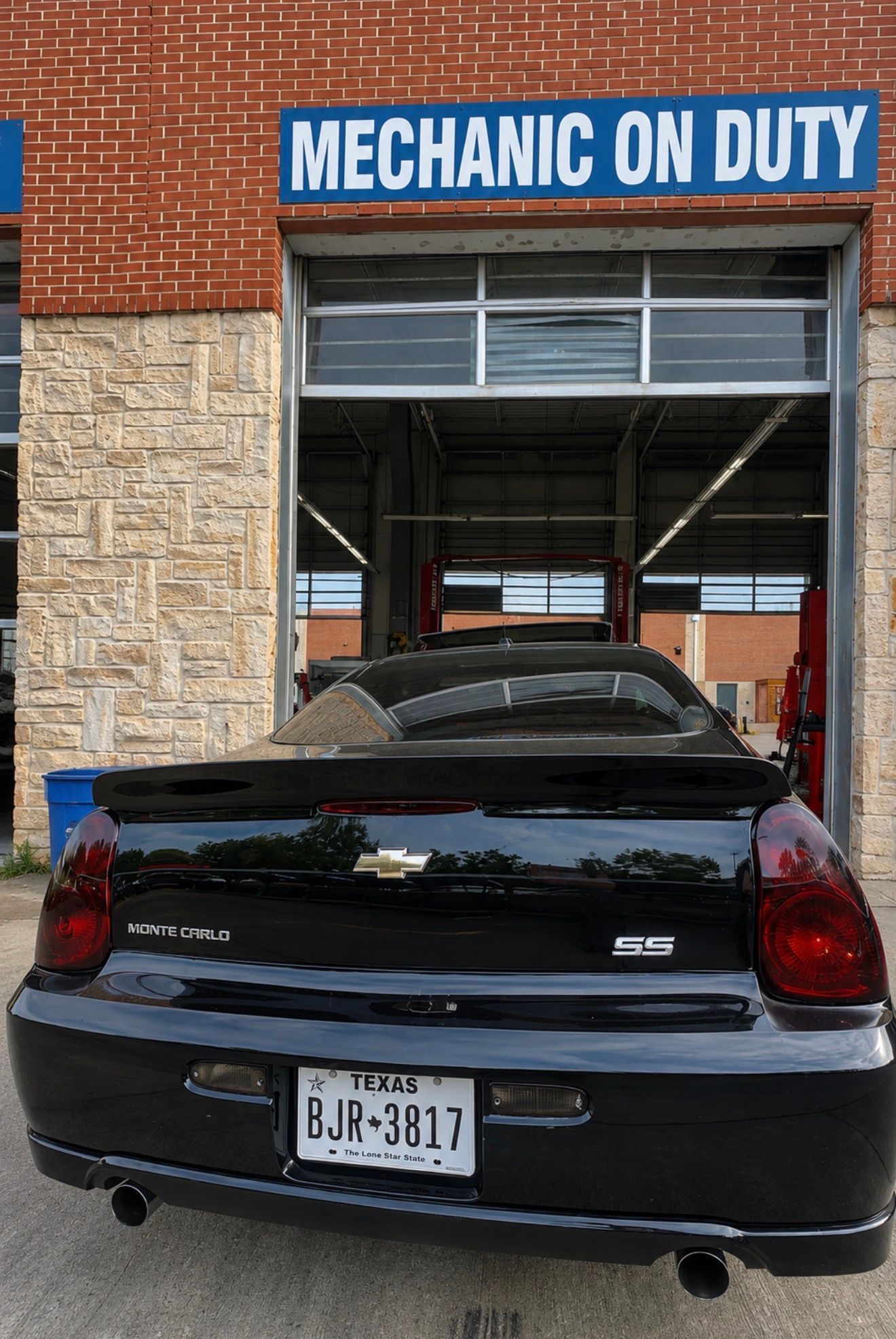 Black Chevrolet sedan parked in front of a garage labeled “MECHANIC ON DUTY”