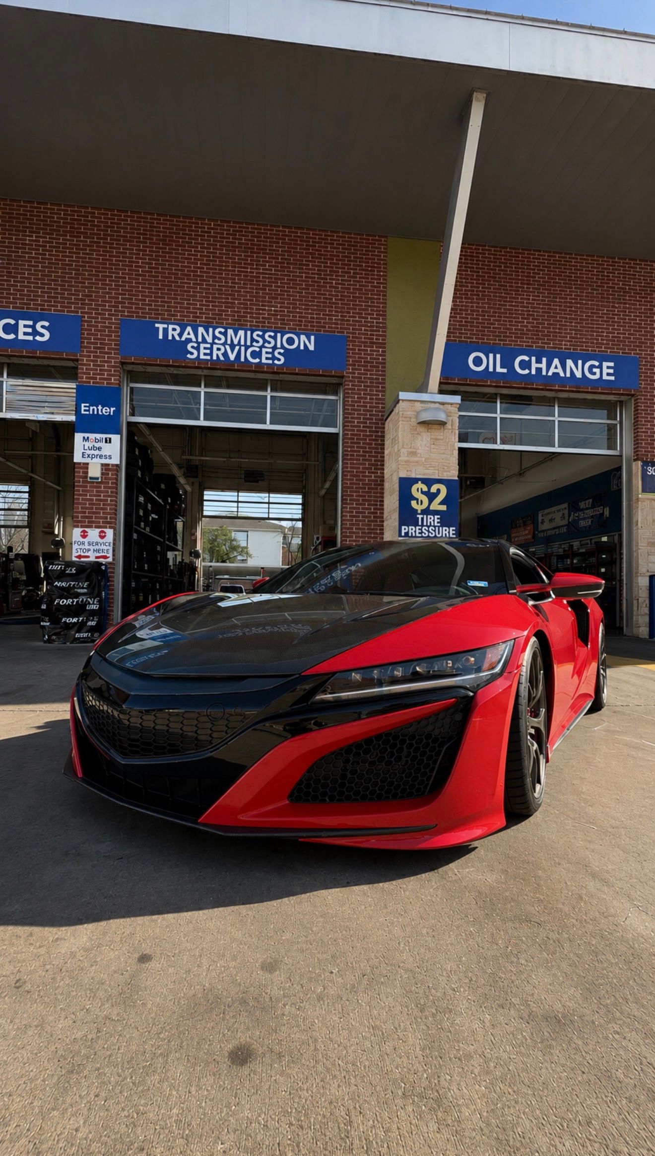 Red sports car parked outside an oil change shop with blue signage.