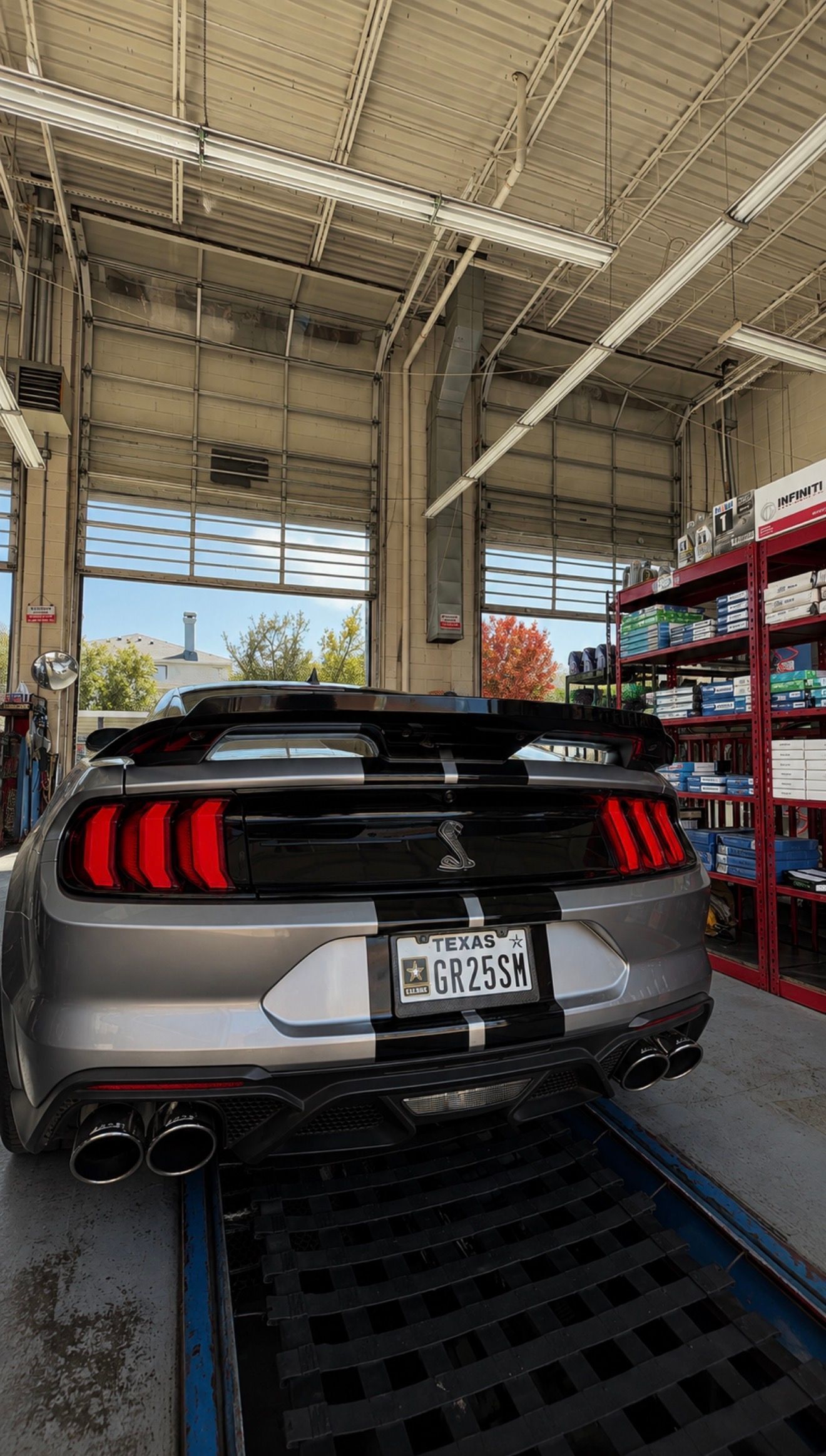 Silver sports car in a service bay, viewed from the rear under a garage roof.