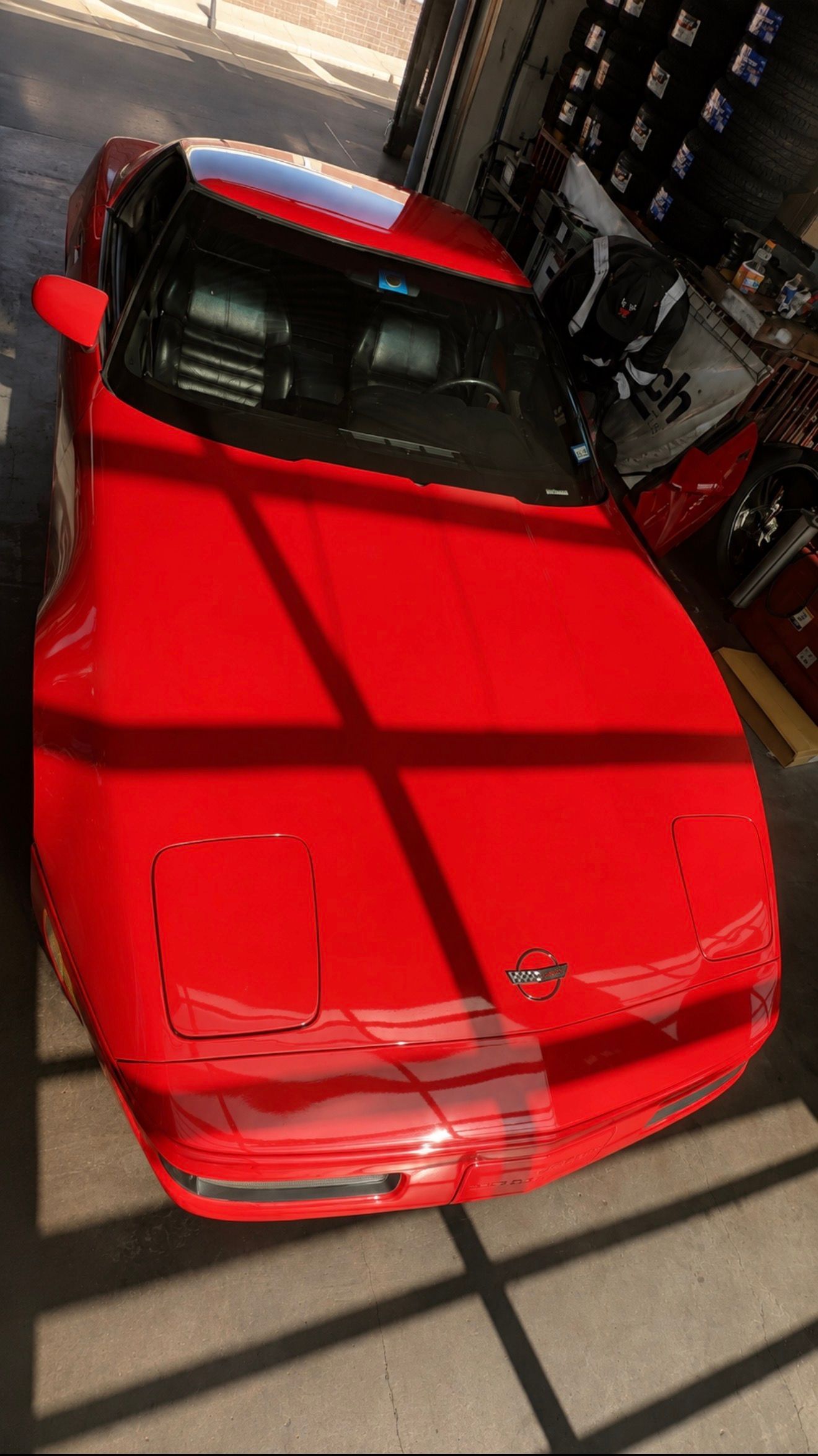 Red sports car parked indoors, viewed from above with strong window shadows across the hood.