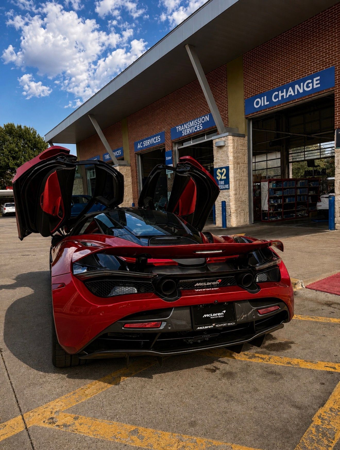Red sports car with doors open outside an oil change shop on a sunny day