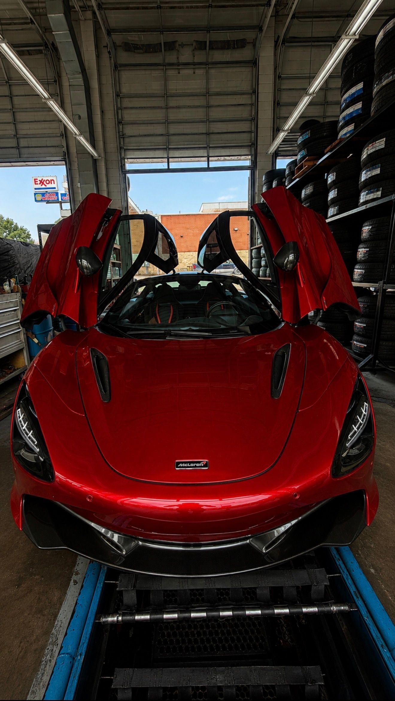 Red sports car with butterfly doors raised, parked inside a transport trailer.