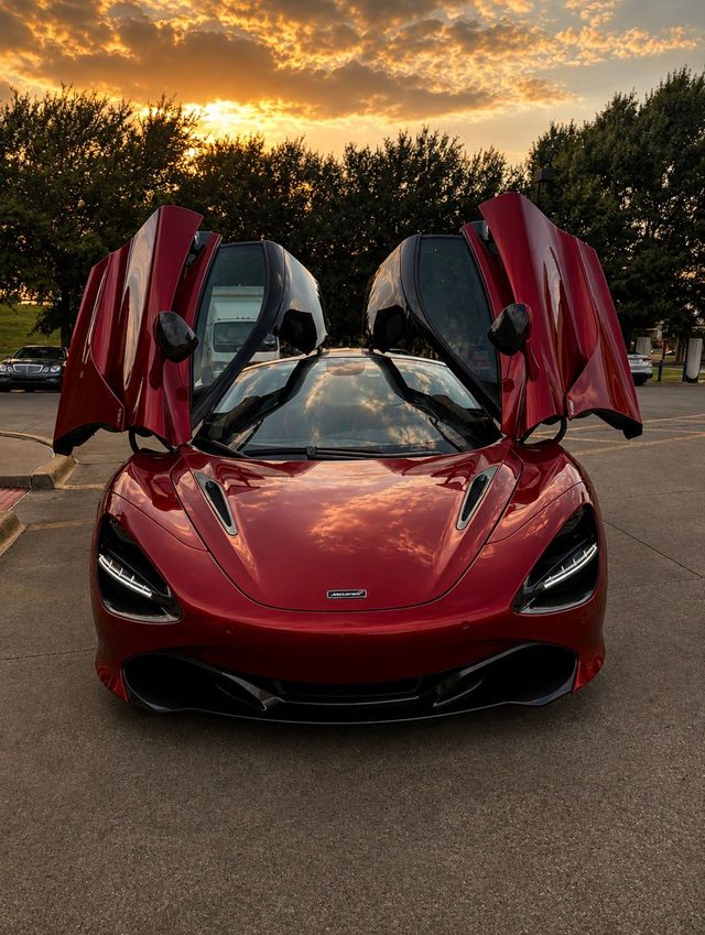 Red sports car with butterfly doors open at sunset in a parking lot
