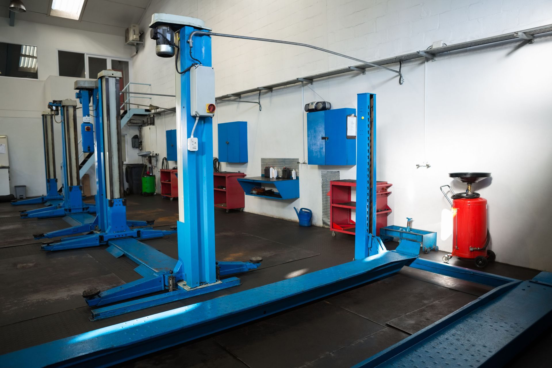An interior view of an auto repair shop featuring multiple blue hydraulic vehicle lifts on a dark floor.
