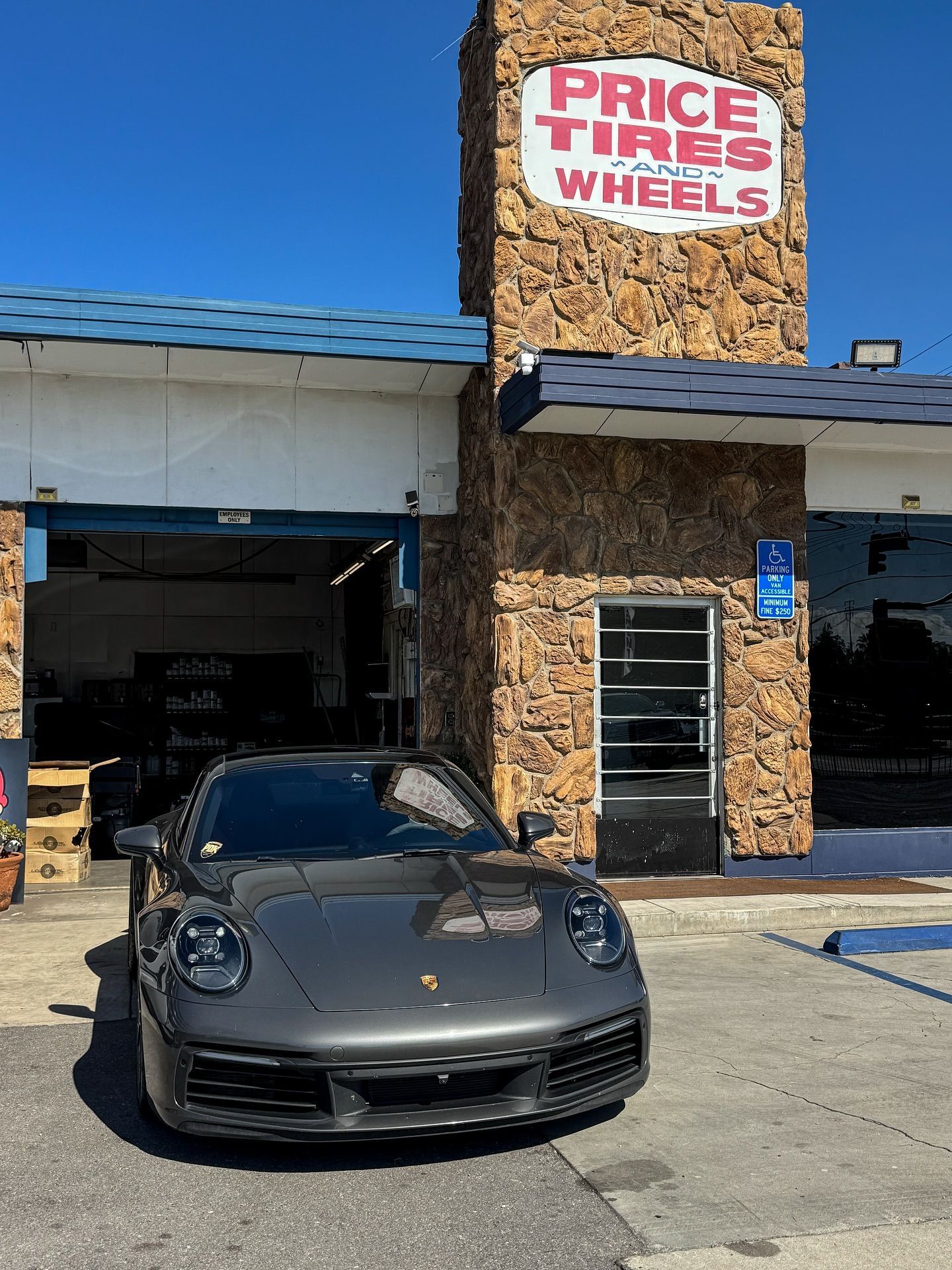 A dark gray Porsche parked in front of a stone building with a sign that reads 