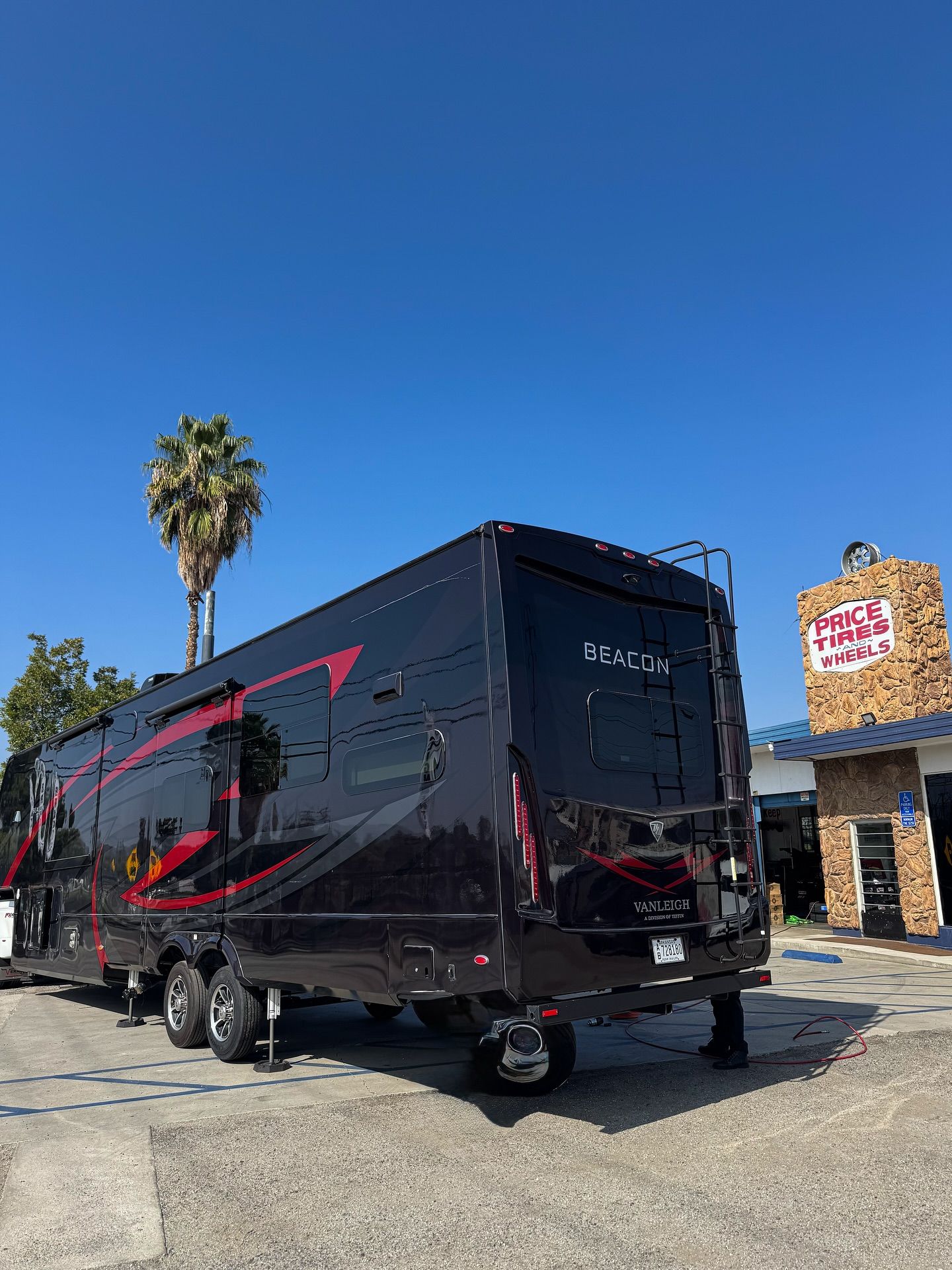 A black toy hauler trailer with red accents parked on an asphalt lot beside a stone-faced building under a clear blue sky.