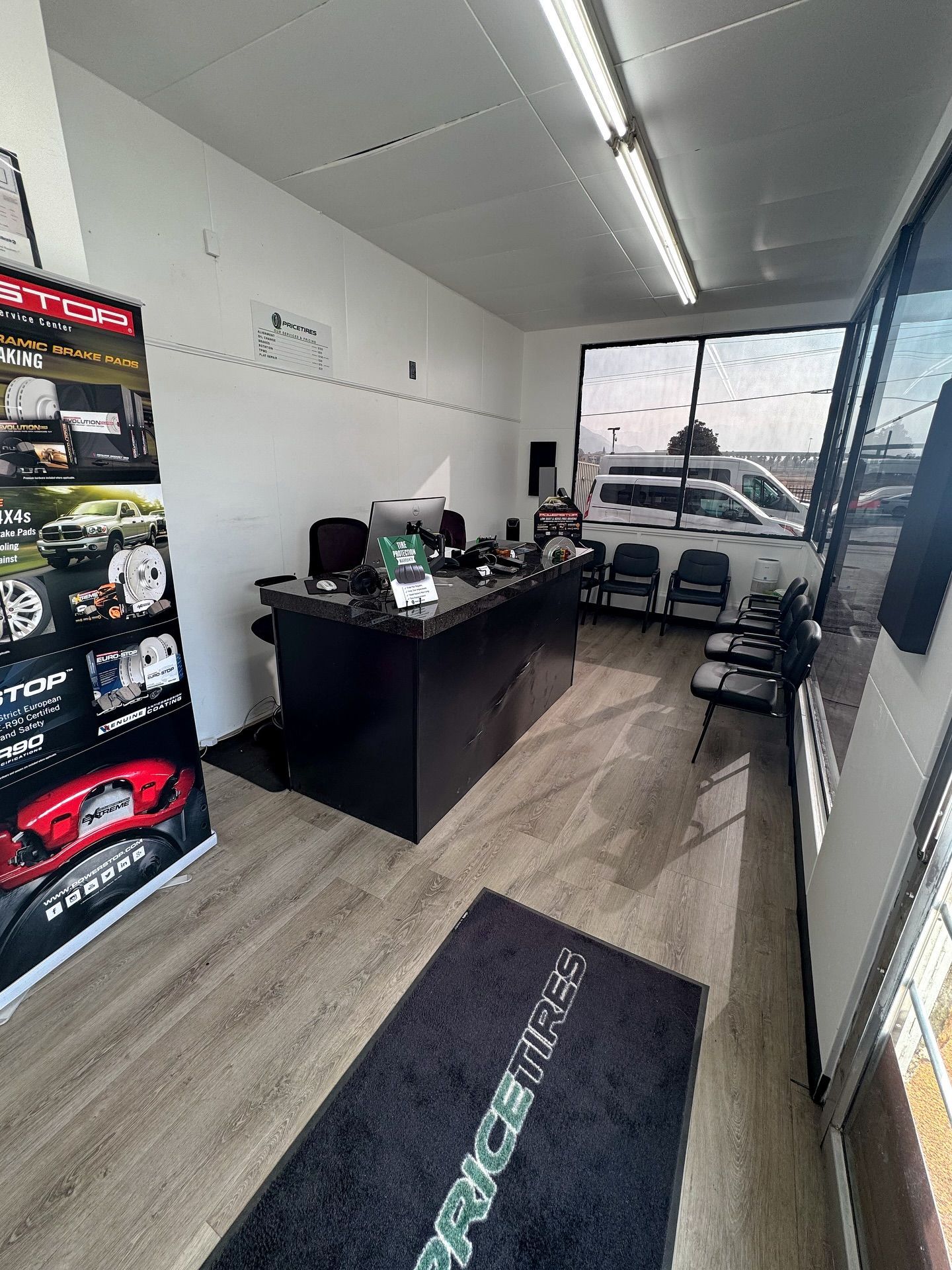 Interior of a tire shop with a black reception desk, wood-look flooring, a branded floor mat, and a large display board.