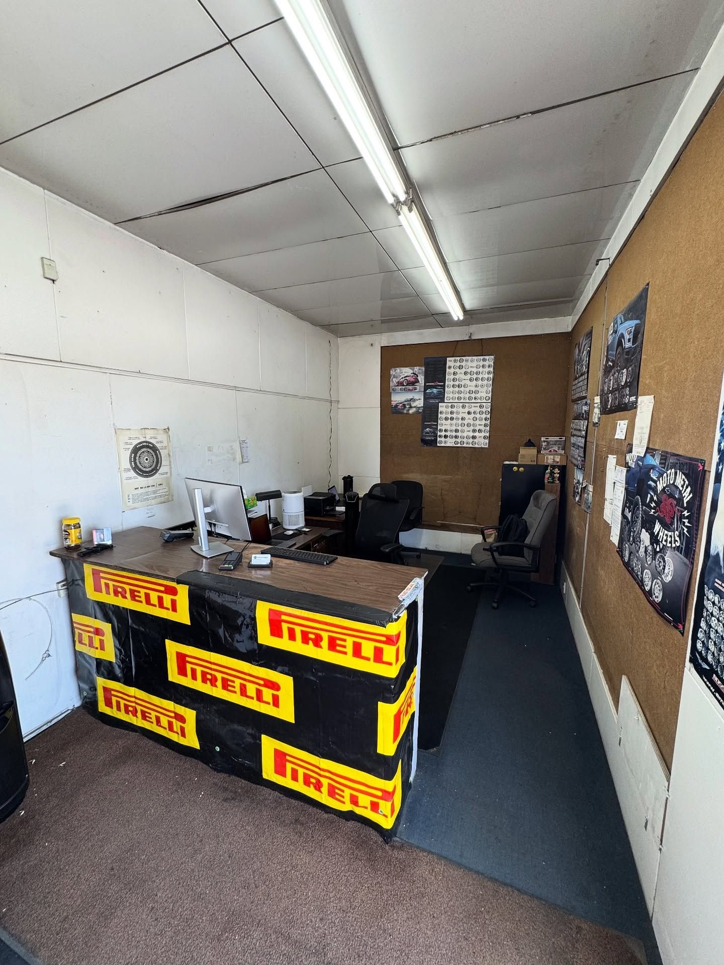 A small office with a front desk wrapped in black and yellow Pirelli signage, a computer, and corkboards on the walls.