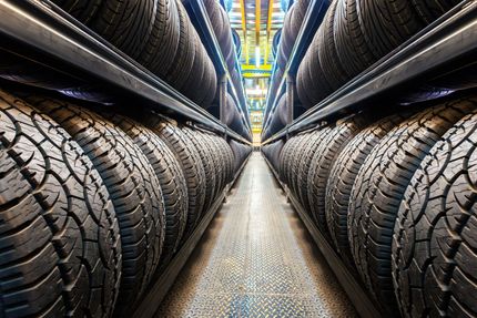 Rows of black car tires stored on metal warehouse shelves along a central aisle.