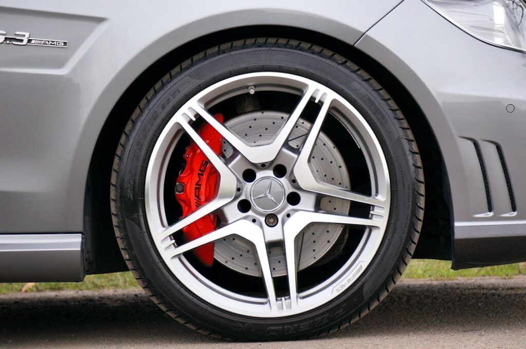 A close-up of a silver Mercedes-Benz car wheel featuring a red AMG brake caliper and a perforated brake disc.