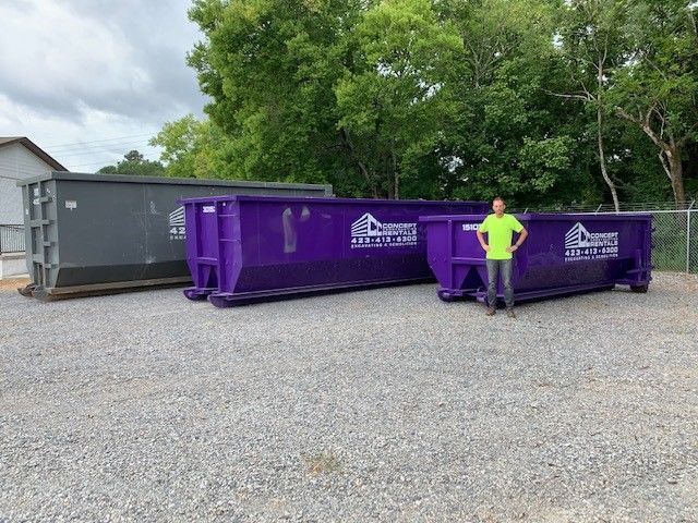 A man is standing in front of two large purple dumpsters.